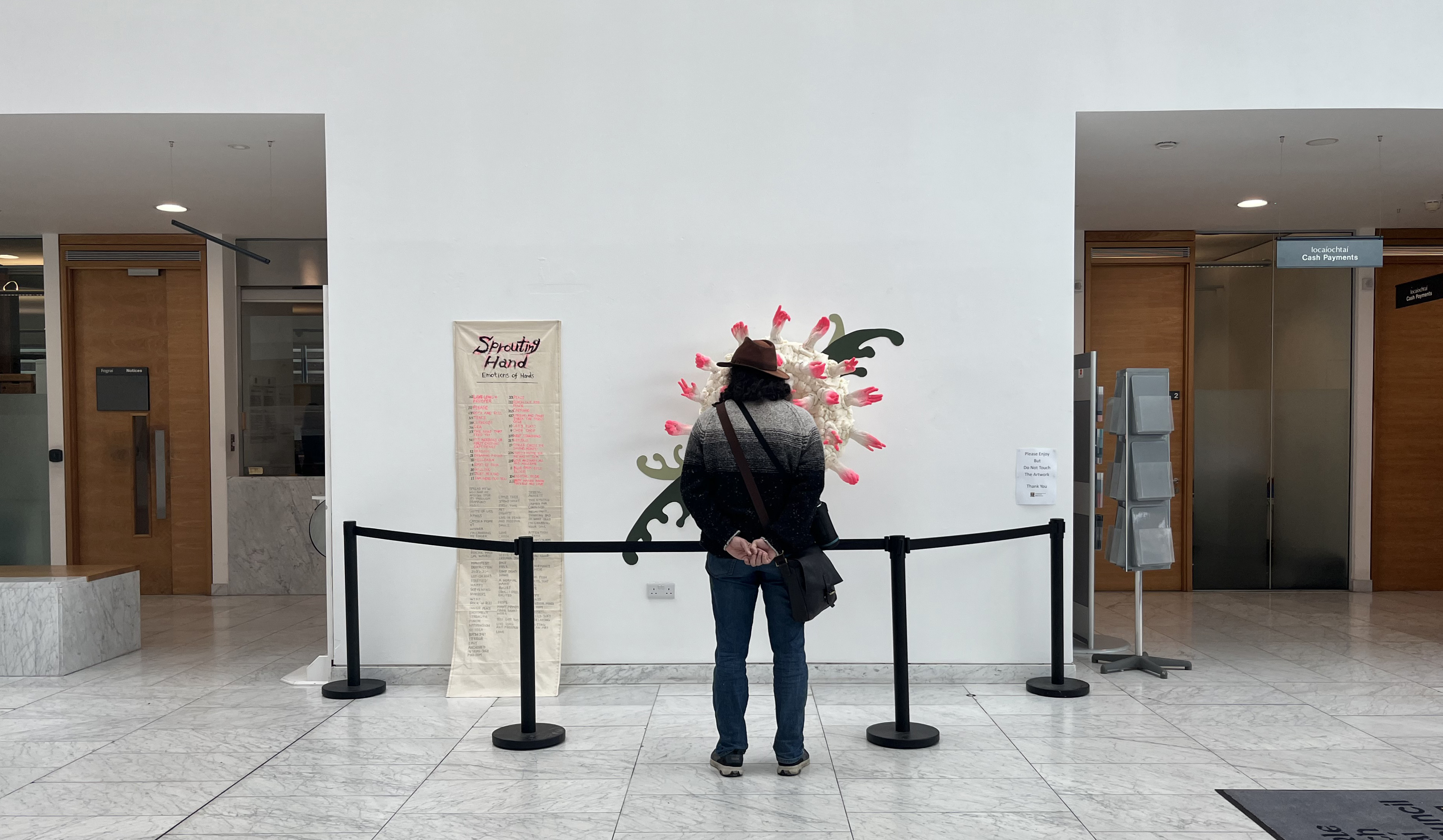 Sprouting Hands Exhibition 2023 - by Seiko Hayase - on the wall of the Atrium, with an audience member looking at the piece