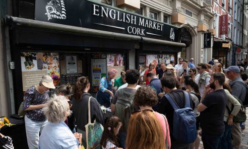 A crowd of people gathered on the street outside entrance to English Market