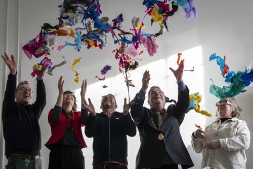 Image Description: All five figures look upwards smiling at a collection of multi-coloured paper pieces released into the air by their hands. The Lord Mayor is discernible by his gold chain of office, fourth from the left. To his right are Michael and Niall wearing dark tops and glasses. Siobhán is between them wearing a magenta jacket and colourful scarf while Deirdre stands to the Lord Mayor's left wearing a white shirt and black and white glasses.